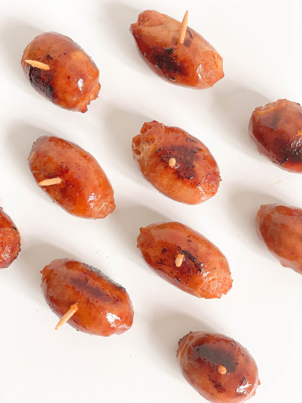 Grilled Taiwanese mini sausages with toothpicks, arranged in rows on a white background. 