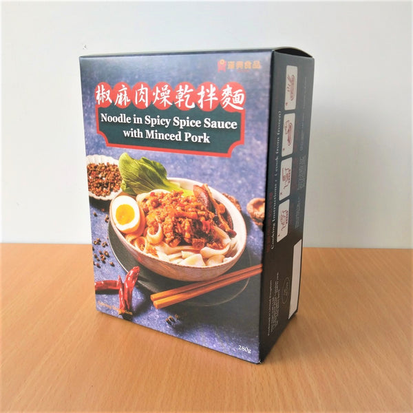 A box of 'Minced Pork Noodles with Chili Sauce' sits on a wooden surface. The ready-to-eat packaging is printed with images of the dish showcasing the noodles, minced pork, poached egg and garnish. Red and gold text on a dark background and food illustrations complete the look.